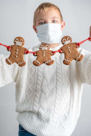 A boy holding Christmas gingerbread men with a masks