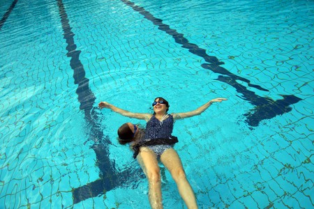 Young beautiful mum together with the beauty a daughter study to float in a swimming pool.