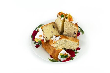 Sliced Easter cake with fondant and candied fruit on a plate on a white background.