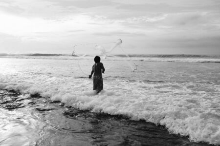 A fisherman throwing his net into the ocean - black and white photoの写真素材