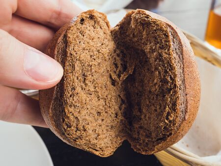 small half-broken round rye bun in hand, closeupの写真素材