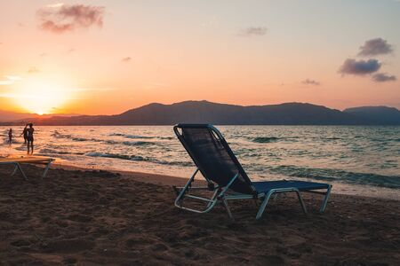 empty beach chair on a sandy beach on a sunset background. The sun sets in the mountains on Crete, Greeceの写真素材
