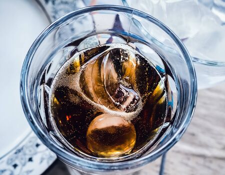 two pieces of ice float in a glass with a dark carbonated drink. Close-upの写真素材
