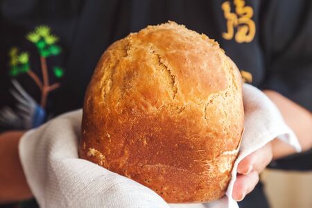 homemade white bread in hands on a white waffle towel, black apron with oriental embroideryの写真素材