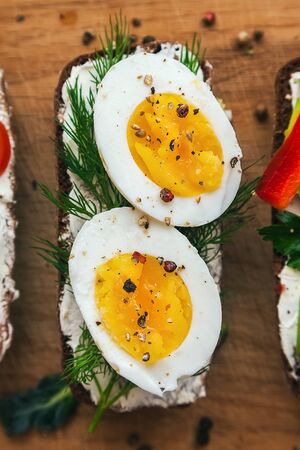 bruschetta on a wooden board: on dark bread, a chicken egg, dill and curd cheese cut in two, decorated with spicesの写真素材