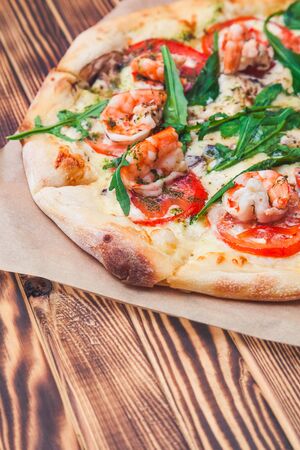 slice of italian pizza with royal prawns, tomatoes, cheese and arugula on a classic dough on a wooden table close-upの写真素材