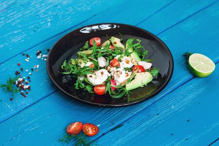 salad of arugula, avocado, cottage cheese, radish and cherry tomatoes on a black glossy plateの写真素材
