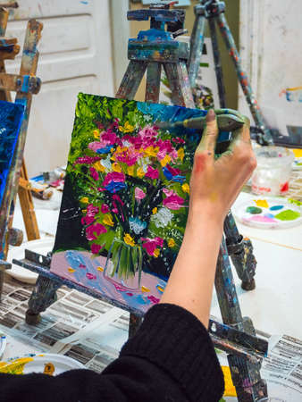 Rostov-on-Don, Russia - February 22, 2020: the artist paints a painting with a palette knife - a bouquet of wildflowers in a vaseのeditorial素材