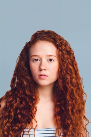 pretty teenage girl with luxurious long curly red hair on a blue background in the studioの写真素材