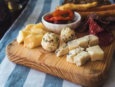 Assorted cheeses and sausages on a wooden board on a table with a linen striped tableclothの写真素材