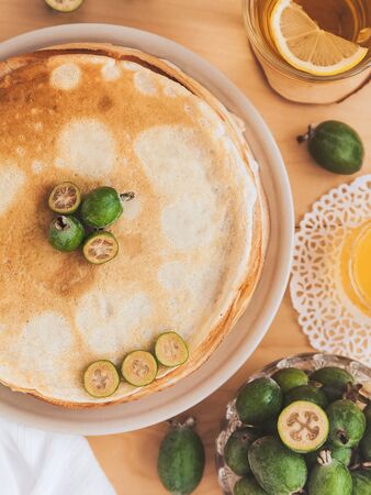 thin large pancakes decorated with feijoa fruits and a cup of green tea with a slice of lemon, acacia honey in a crystal vase on a lace napkin.  Top viewの写真素材