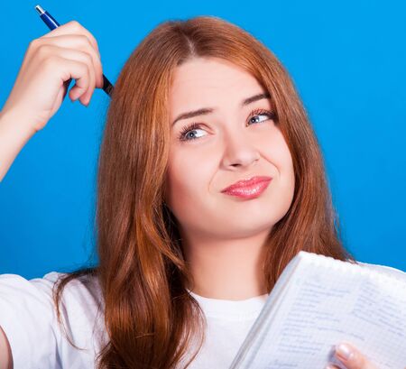 young red-haired girl with blue eyes in a white t-shirt thinks what to write in a notebook. Close-up, skin retouchingの写真素材