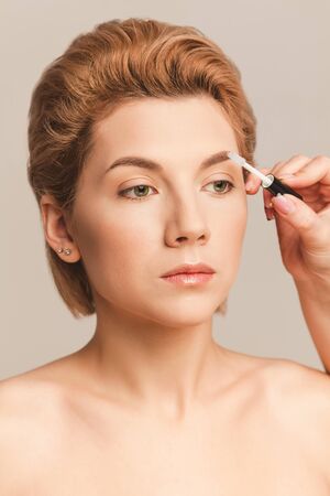 styling eyebrows with a transparent gel. Portrait of a beautiful blonde model on a beige background in the studioの写真素材
