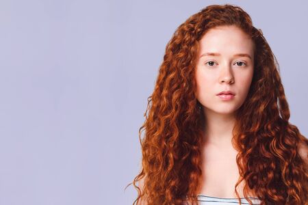 pretty teenage girl with luxurious long curly red hair on a lilac background in the studioの写真素材