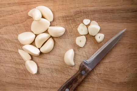one cut and many uncut peeled cloves of garlic on a wooden cutting board and a knife, flat layの写真素材