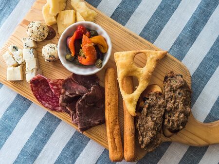 Cheeses, sausages, bruschettas, olives and capers on a wooden board on a table with a linen striped...