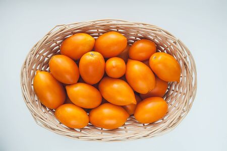 many ripe juicy yellow tomatoes in a light straw basket close-upの写真素材