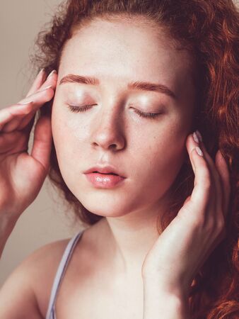 a beautiful girl with freckles and curly hair washed her face and closed her eyes. Skin hydration concept. No makeup, close-up faceの写真素材