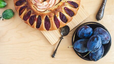 plum cake decorated with a rose from apple slices, an old spoon and a saucer with fruitの写真素材