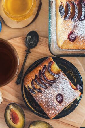 a square slice of plum pie on a round black antique plate, acacia honey, a vintage teaspoon and a...