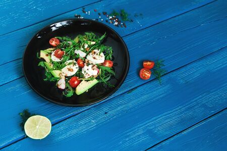salad of arugula, avocado, cottage cheese, radish and cherry tomatoes on a black glossy plateの写真素材