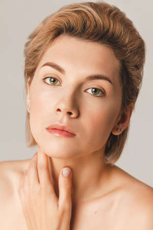 Attractive blonde model with a short haircut and green eyes looks at the camera. Close-up, retouch, shot in the studio on a light background. Skin Care Concept 25+の写真素材
