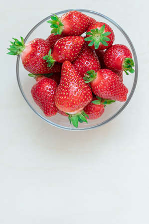 ripe strawberries of different sizes and varieties in a glass plate on a light wooden background, flat lay, copy spaceの写真素材
