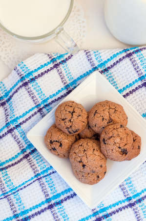 oatmeal cookies on a square white plate on a white waffle towel with blue stripes, a transparent cup with milkの写真素材