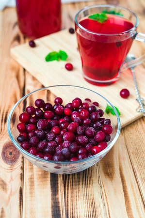frosted wild cranberries in a glass cup and a mug with berry fruit juice on a bamboo board close-upの写真素材