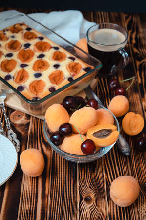 ripe apricots and cherries in a glass transparent bowl on a background of cake and coffee on a wooden table - seasonal berries baked goods for breakfastの写真素材
