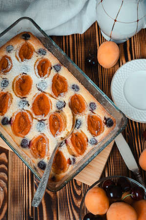 vintage spoon in apricot curd cake decorated with icing sugar and seasonal berries on a wooden table, flat layの写真素材