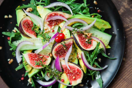 salad on a black matte plate: arugula, figs, avocado, red onions, cucumbers, walnuts, viburnum, thyme, spicesの写真素材