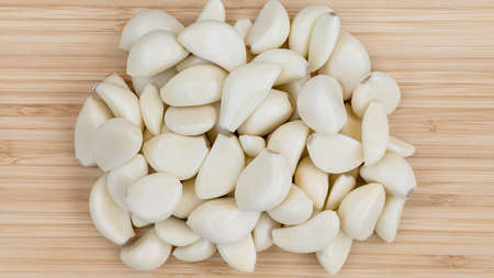 many peeled white cloves of garlic on a bamboo cutting boardの写真素材