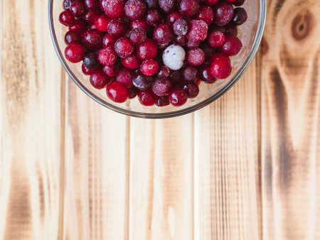frozen wild cranberries in a glass cup on a wooden table, flat lay, copy spaceの写真素材