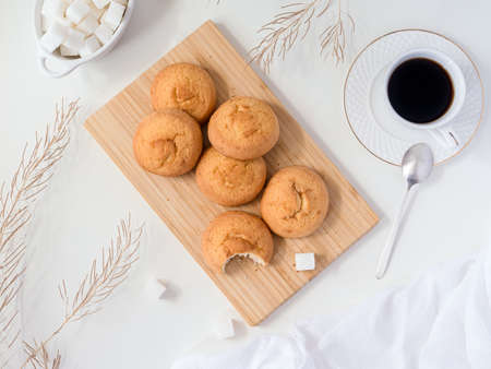 flat lay - a delicious round biscuit cookie on a bamboo cutting board on a white background, a cup of coffee, refined sugar, sprigs of dry grass, a waffle towel, a silver vintage teaspoon.の写真素材