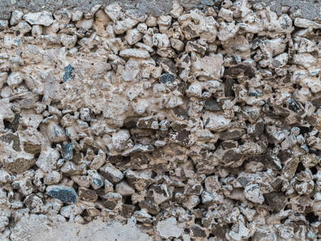 A fragment of an old concrete wall with gravel. Cracks, spots and pits close up.の写真素材