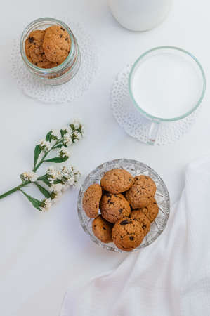oatmeal cookies with chocolate chips on a crystal plate, a mug of milk, a glass bottle and a wildflower - flatleyの写真素材
