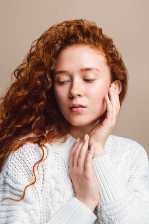 beautiful red-haired girl in a white sweater posing on a beige background in the studioの写真素材