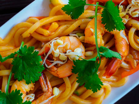 Wok with prawns, udon noodles and mung bean, garnished with cilantro sprigs close-upの写真素材