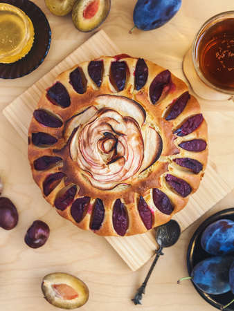 round cake decorated with slices of plums and apples. Autumn still life with fresh fruits and tea on a light wooden tableの写真素材