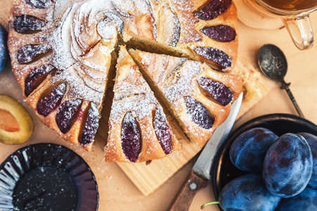 still life: round plum cake decorated with icing sugar, a cup of black tea and a saucer with fruitの写真素材
