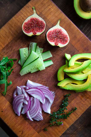 figs, avocado, cucumber, arugula, red onion, thyme on a cutting wooden board close-up - salad ingredientsの写真素材