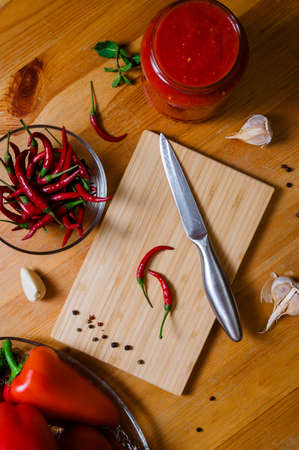 two small hot peppers on a bamboo cutting board - preparation for the sauce. Paprika, tomatoes, garlic and spices on a wooden tableの写真素材