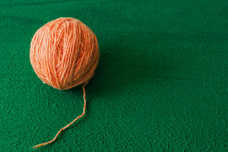 a ball of woolen thread in peach color for knitting on a green background close-up, copy spaceの写真素材