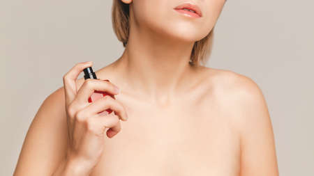 perfume water in a red bottle in the hands of a blonde girl, brought to her neckの写真素材