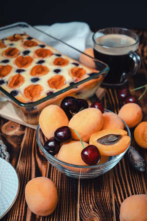 still life with a glass bowl with apricots and cherries, cottage cheese pie, coffee on a wooden table close-upの写真素材