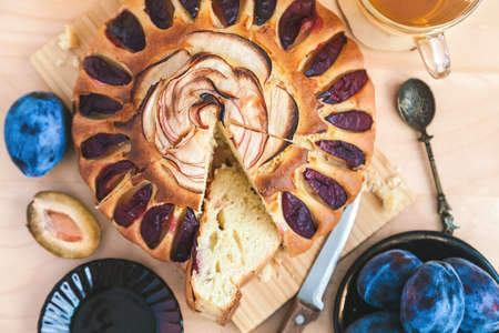 still life: a round plum cake, cut into pieces, decorated with a rose from apple slices, a cup of black tea and a saucer with fruitの写真素材