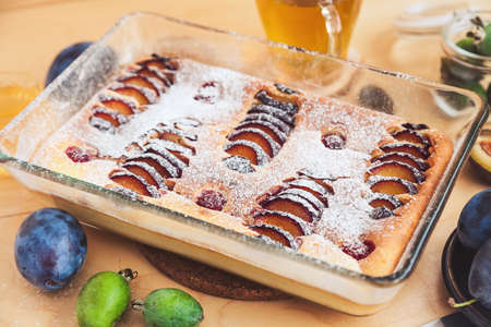 cottage cheese pie with slices of plum and raspberries decorated with icing sugarの写真素材