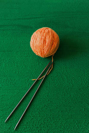 a ball of peach colored woolen threads and two knitting needles on a green background close-up, copy spaceの写真素材
