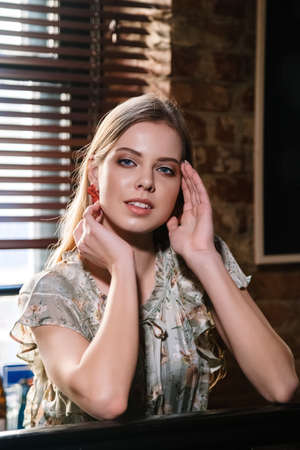 beautiful girl with natural blond hair and blue eyes is sitting at the bar counter and smilingの写真素材
